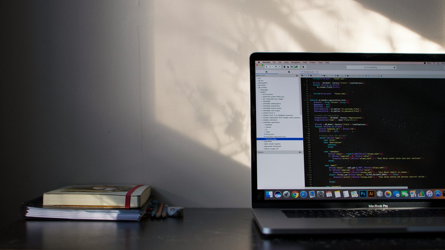 A laptop open on a wooden desk showing lines of code, with a notebook and a mug beside it