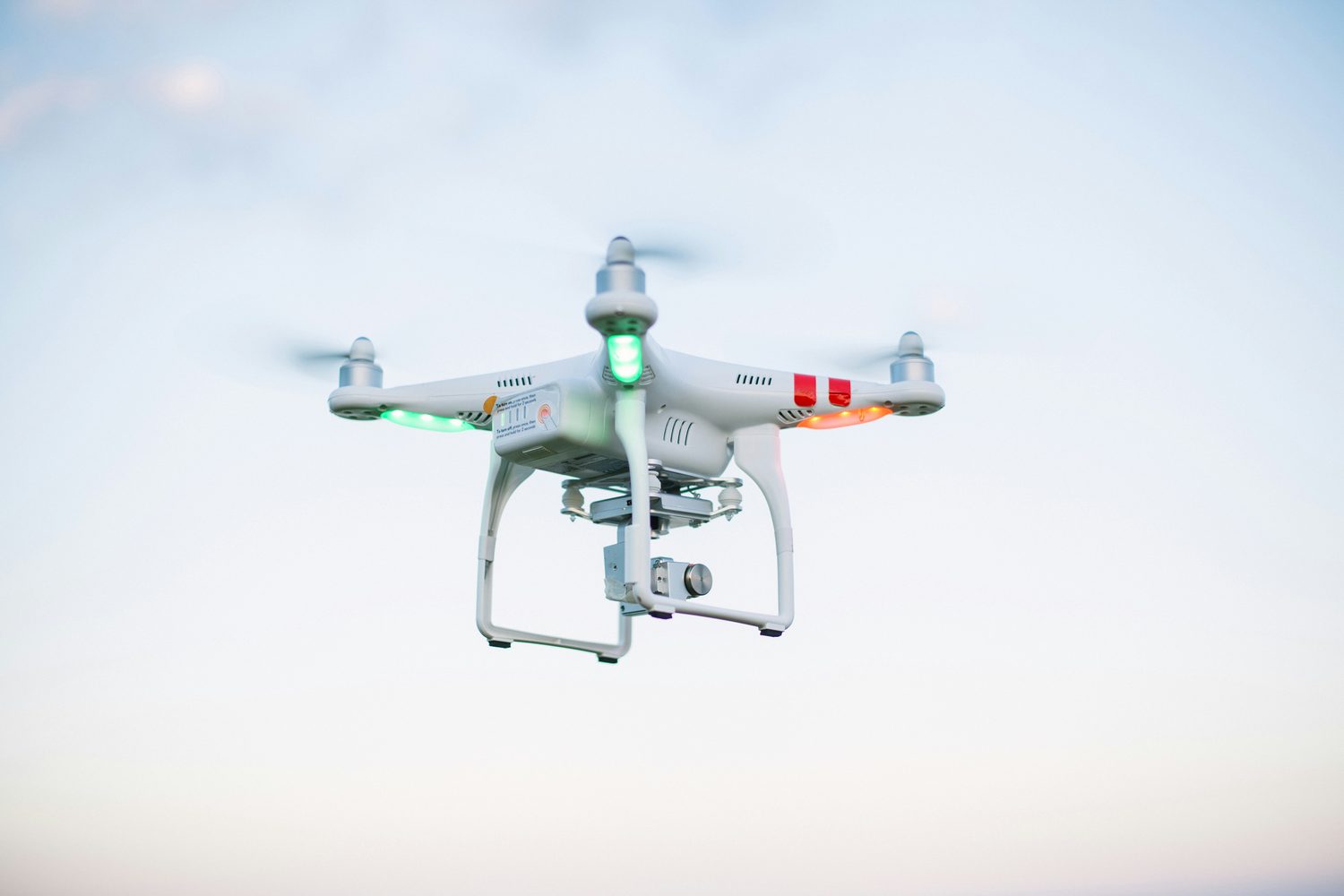 A four-rotor camera drone hovering against a pale overcast sky